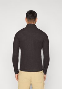 Top negro de manga larga con un patrón de punto texturizado, cuello alto simulado y diseño ajustado. Presenta un acabado suave y una forma entallada.