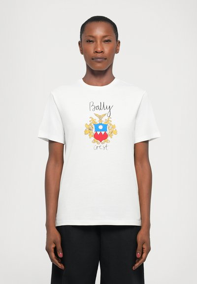 Fehér pamut póló, színes Bally címer grafikával, kék, piros és arany részletekkel, kerek nyakkal és rövid ujjakkal.