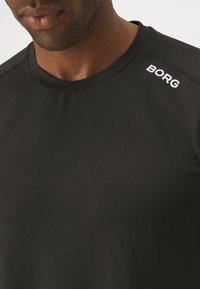 Fekete sportpóló sima anyagból. Kerek nyakkivágással rendelkezik, és a "BORG" felirat fehér színben látható a vállon.