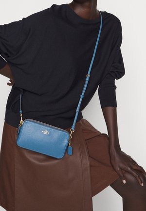 Blue leather crossbody bag with zipper, gold hardware, and textured finish, featuring an adjustable strap and a small tag.