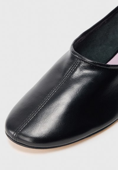 Scarpa in pelle nera con una texture liscia, punta rotonda, dettagli delle cuciture sottili lungo la parte superiore e una suola sottile e piatta.