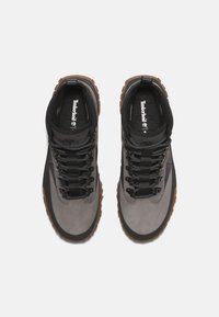 Szaro zamszowa i syntetyczna cholewka z czarnymi akcentami, teksturowane sznurówki oraz brązowa gumowa podeszwa. Posiada wyściełany kołnierz dla większego komfortu.