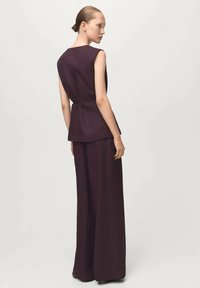 Bordowa, bezrękawnik z peplum, w połączeniu z szerokimi spodniami, oba wykonane z fakturowanej tkaniny. Prosta, nowoczesna sylwetka.