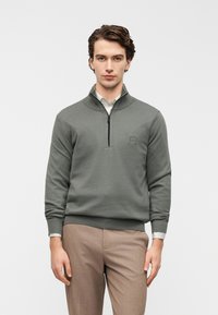 Γκρι πουλόβερ με φερμουάρ μέχρι το λαιμό, φτιαγμένο από μαλακό ύφασμα. Διαθέτει ριμπ μανσέτες και τελείωμα, με μικρό λογότυπο στο στήθος.