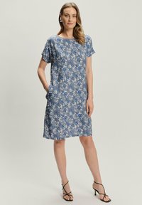 Niebieska sukienka z krótkim rękawem w wzory, z kieszeniami, z kwiatowym wzorem w odcieniach niebieskiego i białego, wykonana z lekkiego materiału.
