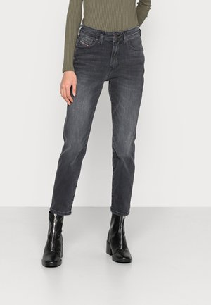 Personne portant un jean noir délavé taille haute, un haut côtelé manches longues olive, et des bottines noires à talon avec fermetures éclair à l'avant.