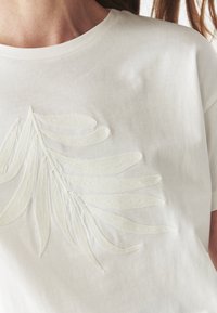 Biela bavlnená tričko s textúrovaným, vyšívaným dizajnom listu v jemnej, off-white farbe. Okrúhly výstrih a voľný strih.