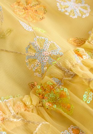 Tessuto giallo con motivi floreali di paillettes iridescenti e sezioni arricciate e svolazzanti che creano texture e dimensione.