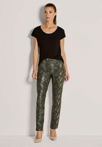 Zwarte top met korte mouwen gecombineerd met groene en zwarte slangenprint broek, met een slim fit en een gladde textuur, aangevuld met beige hakken.