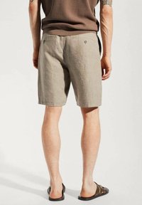 Herren Leinen-Shorts in Hellgrau. Mit zwei Gesäßtaschen mit Knöpfen, lockerer Passform und strukturierter Oberfläche. Kombiniert mit dunklen Slide-Sandalen.