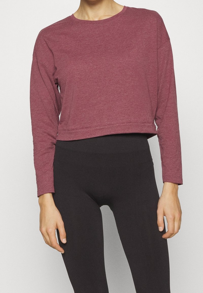 Top corto a maniche lunghe color marrone scuro in tessuto morbido, con scollo rotondo e vestibilità rilassata, abbinato a leggings neri a vita alta.