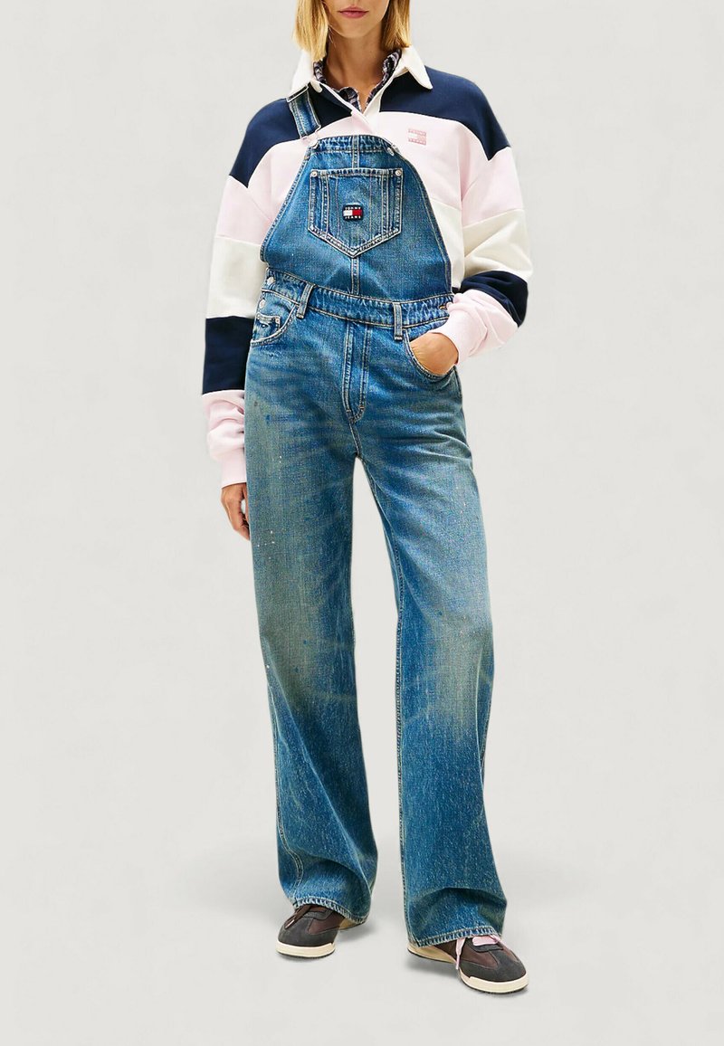 Jeansowe ogrodniczki w jasnoniebieskim kolorze z szerokimi nogawkami, przednią kieszenią i regulowanymi paskami. Połączone z bluzą w kolorowe pasy.