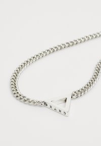 Collier en chaîne argentée avec un pendentif triangulaire doté d'un centre creux et de l'inscription "BRAND" gravée, présentant une finition métallique polie.