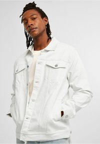 Weiße Jeansjacke mit klassischem Kragen, vorderen Druckknöpfen, zwei Brusttaschen und Seitentaschen. Glatte Textur mit lockerer Passform.