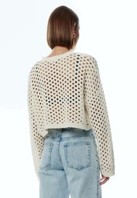 Pull crème au crochet, coupe ample, avec de grands motifs à mailles ajourées et manches longues, associé à un jean bleu clair taille haute.