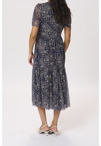 Marineblaues Kleid mit gestuftem Rock, transparenten Ärmeln und floralem Muster in Creme. Hat ein tailliertes Oberteil und einen fließenden Saum.