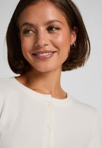 White ribbed button-up top with a round neckline and small buttons. Smooth texture and relaxed fit, featuring subtle stitching details.