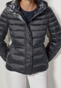 Puffetjakke i mørkegrå med en skinnende, hættekrave. Har en lynlåslukning foran, horisontal quiltet struktur og sidelommer.