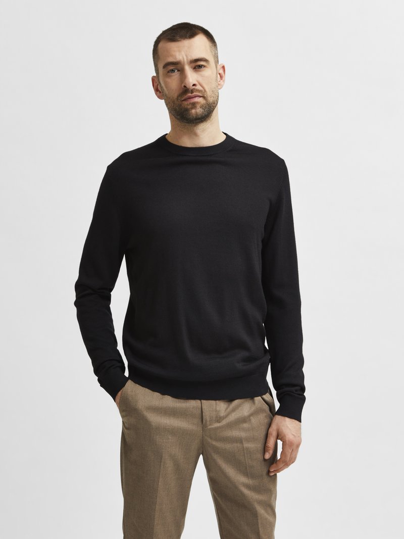Black long-sleeve sweater made of soft fabric with a round neckline and ribbed cuffs, paired with light brown pleated trousers.