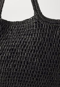 Czarna pleciona torba tote wykonana z teksturowanego materiału, z wplecionym uchwytem i usztywnionym kształtem, ukazująca misterny detal tkactwa.