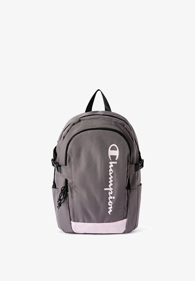 Mochila de tela gris con forma redondeada, que cuenta con un compartimento grande, bolsillos laterales y un detalle rosa en la parte inferior, con la marca "Champion".