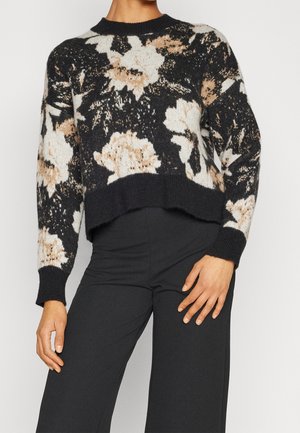 Zwarte, beige en witte gebloemde gebreide trui met ribgebreide manchetten en zoom, gecombineerd met zwarte hoge taille, wijde broek.