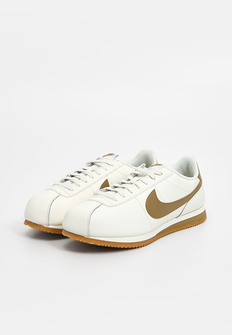 Weiße Nike-Sneaker mit einem glatten Lederobermaterial, braunem Swoosh-Logo, runder Zehenpartie und hellbrauner Gummisohle. Schnürsenkel im Standardlayout.