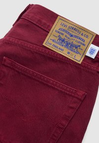 Μοντενέ μπορντό τζίν Levi's διπλωμένο, δείχνει πίσω τσέπη και ταμπελάκι από δέρμα σε ταμπά χρώμα με μπλε κείμενο και λογότυπο αλόγου, μέγεθος W32 L.