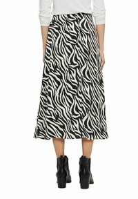 Zwart-witte jurk met zebraprint in maxi-lengte met een vloeiende uitstraling. Beschikt over een platte tailleband en is gecombineerd met zwarte enkelboots.