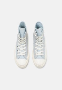 Wysokie sneakersy w jasnoniebieskim zamszu z białymi gumowymi czubkami, płaskimi białymi sznurówkami i srebrnymi oczkami. Charakteryzują się gładką teksturą i minimalistycznym designem.