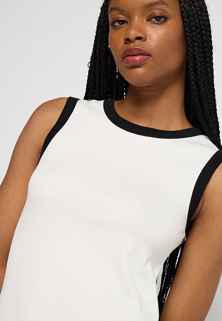 Biała bluzka bez rękawów z czarnymi wykończeniami wokół dekoltu i otworów na ramiona, charakteryzująca się miękką fakturą i dopasowanym krojem.