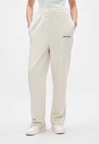 Ανοιχτό μπεζ φόρμες με ελαστική μέση, πλευρικές τσέπες και κεντημένο λογότυπο "Calvin Klein" στην αριστερή πλευρά. Λείο υλικό.
