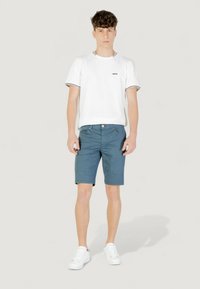Camiseta blanca de cuello redondo con un pequeño logo negro, pantalones cortos azules y zapatillas blancas. Los pantalones cortos tienen bolsillos laterales y un simple dobladillo.