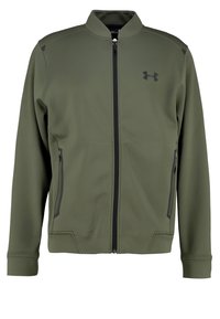 Veste zippée vert olive avec fermeture éclair noire, deux poches latérales zippées et logo Under Armour sur la poitrine gauche.
