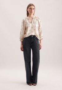 Lys beige bluse med blomstermotiv og V-udskæring, parret med mørkegrå brede bukser, præsenteret mod en neutral baggrund.