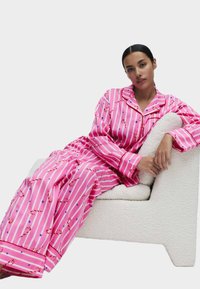 Różowy piżama w paski z wzorami cukrowych lasek i gwiazd. Miękka tkanina. Luźna bluzka z kołnierzykiem, długie spodnie i szerokie mankiety.