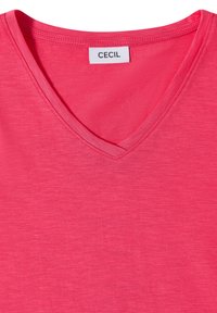 T-shirt rose vif à col en V avec une étiquette blanche portant la mention « CECIL » cousue dans la nuque à l’intérieur.