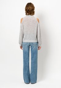 Grauer Strickpullover mit Schulterausschnitten, lockerer Schnitt und gerippten Bündchen. Kombiniert mit hoch taillierten, hellblauen weiten Jeans.