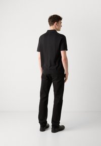 Čierne polo tričko s krátkym rukávom a rebrovaným golierom a manžetami, v kombinácii s čiernymi nohavicami a topánkami, zobrazené zozadu. Minimalistický dizajn.