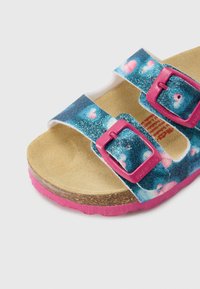 Särav sinine ja roosa sandaal, millel on kaks reguleeritavat rihma roosade pandaldega, korkpõhjaga tallal ning roosast kummist tallaga.