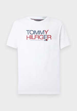 White cotton t-shirt featuring "TOMMY HILFIGER" logo in red and blue. Classic crew neck, short sleeves, and straight hem design.