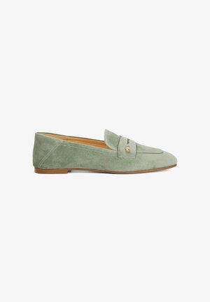 Mocassins en daim vert avec un bout arrondi, présentant un design cousu et un petit accent doré à l'avant. Semelle plate marron.