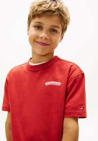 Rød bomuld t-shirt med rund halsudskæring og korte ærmer. Markant hvid "TOMMY" logo på brystet og et lille logo detalje på ærmet.