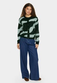 Grön och ljusblå randig stickad cardigan med rund hals, svarta knappar och ribbade ärmslut, kombinerad med vida blå denimbyxor.