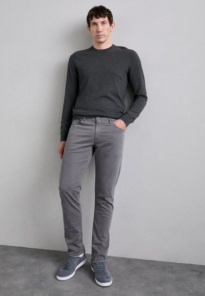 Suéter de lana gris, chinos grises y zapatillas grises. El atuendo presenta un diseño ajustado y una textura sutil, sin patrones ni logotipos visibles.