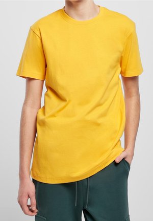 T-shirt en coton jaune à manches courtes, col rond et coupe décontractée, associé à un pantalon de survêtement vert avec poches.
