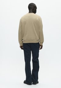Beige sweatshirt med rund hals og ribbede manchetter, parret med mørkeblå brede bukser. Glat tekstur, minimalistisk design og ingen synlige mønstre.