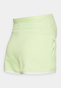 Calções de algodão verde claro com uma cintura elástica, bolsos laterais e um acabamento branco ao longo da barra. Textura suave e design casual.