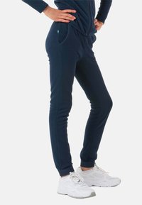Mørkeblå fleece joggers med sidelommer, tapered design, ribbede manchetter og et lille accentmærke. Sammen med hvide sportssko.