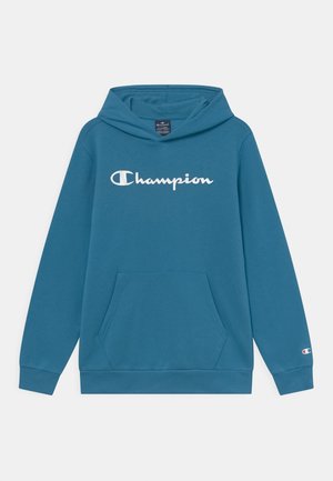 Sweat à capuche bleu Champion avec poche kangourou à l'avant, logo Champion blanc sur la poitrine et petit logo sur le bord de la manche gauche.
